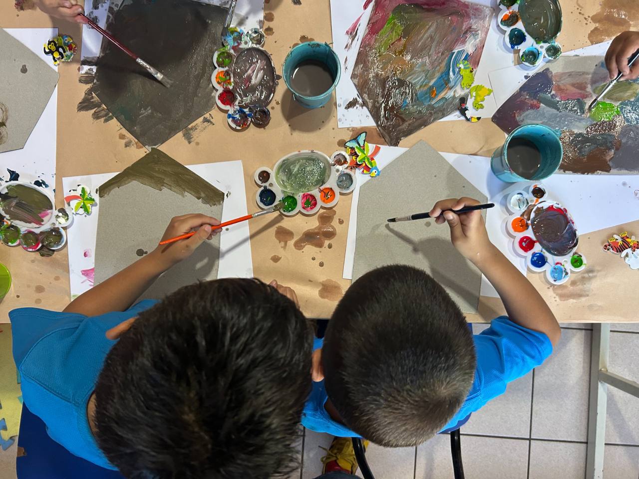 Niñas y niños pintando en una mesa durante un taller de arte
